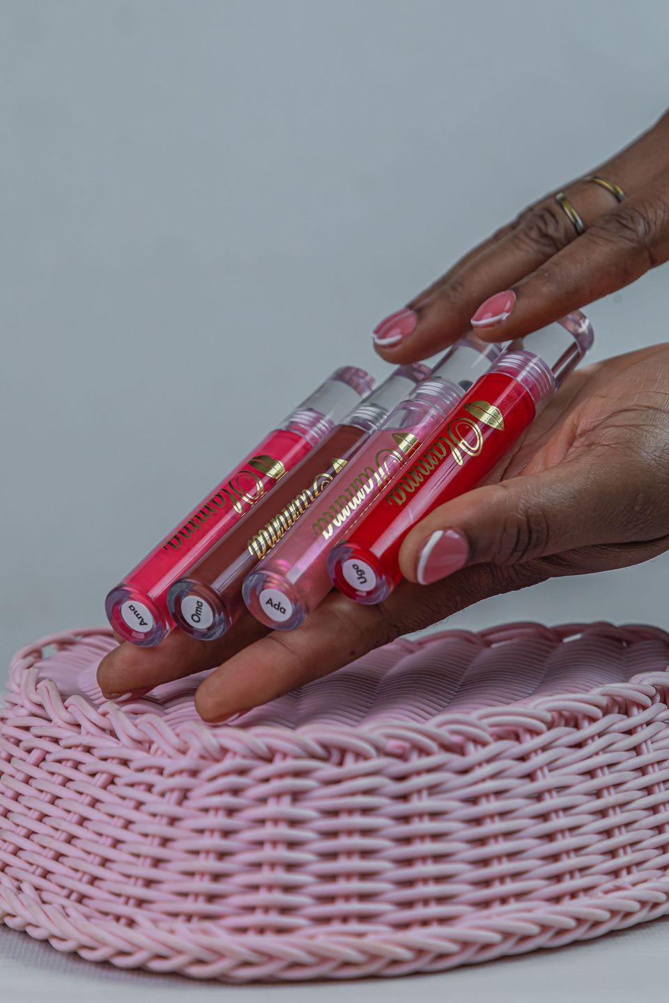 Four OLAMMA gloss tubes resting on a pink woven basket